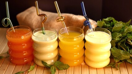  Juices , vibrant ,twisty straws rest on wooden surface with scattered mint leaves. Fun, refreshing...