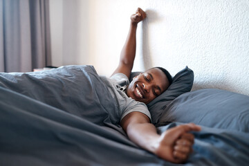 Wake up, stretching and black man on bed in morning for relaxing, resting and sleeping in bedroom. Apartment, happy and person with smile, blanket and comfortable for health, peace and calm for nap