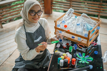 hijab woman posing at camera while painting recycled plastic bottle waste