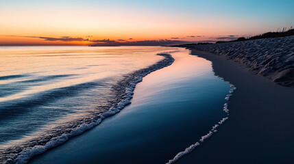 Fototapeta premium Serene sunset over a calm ocean with gentle waves lapping against a sandy beach shoreline under a colorful sky