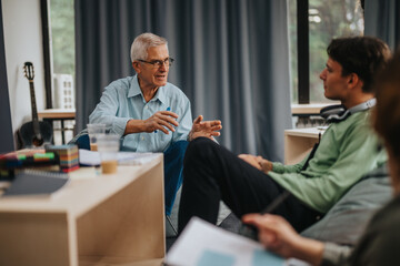 Obraz premium A senior professor engages with students in an informal classroom environment. The atmosphere appears relaxed, encouraging open communication and collaborative learning among the group.