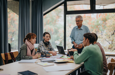 A group of university students engaged in collaborative work on a project, receiving guidance from a senior professor in a modern classroom setting.