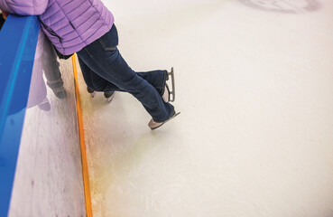 Ice skater leaning against rink barrier while standing on skates, wearing purple jacket and jeans...
