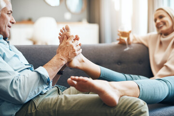 Home, mature and couple with foot massage and care together on sofa with love and smile. Wine,...
