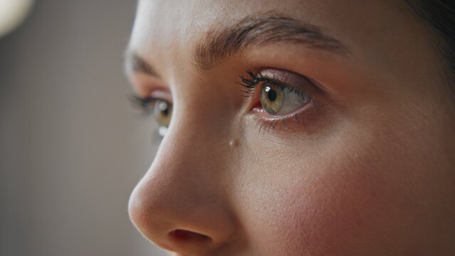Closeup girl eyes looking straight at home. Unknown woman green eye blinking