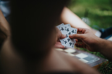 Close-up of hands holding playing cards, engaging in a game outdoors. Perfect for concepts of strategy, leisure, and social interaction.