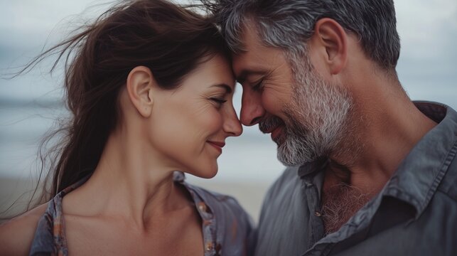 Close-up of a happy middle-aged couple with the beach in the background. The man and woman pressed their foreheads to each other, their faces expressing tenderness and love. - Powered by Adobe