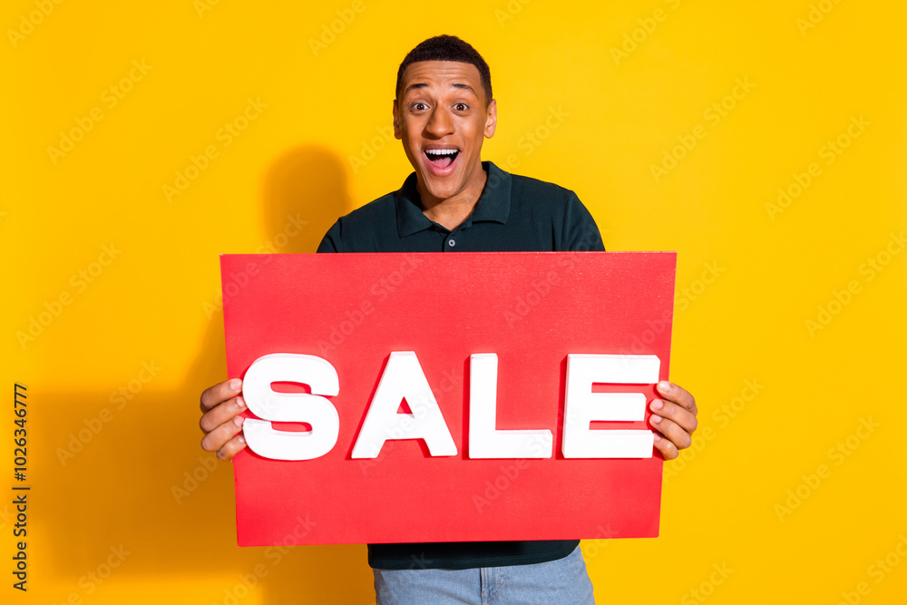 Wall mural Photo portrait of attractive young man hold sale plate excited dressed stylish green clothes isolated on yellow color background