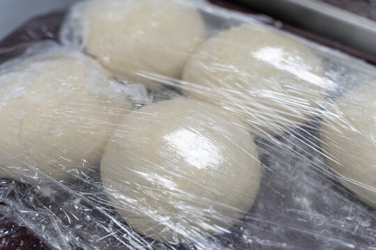 The dough stands on the oven under cling film. A few balls of bread dough on the production table. - Powered by Adobe