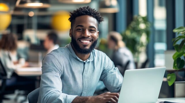 A man with a big smile is sitting at a desk with a laptop