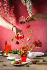 Bartenders pouring ingredients into iced strawberry cocktail with flying berries and mint