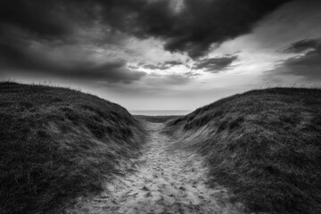 A narrow sandy path between grassy hills leading to a dark overcast sky by the sea