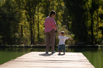 mother and son walk on a wooden footbridge over a lake