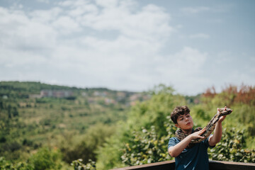 A young girl confidently handles and plays with pet snakes in a verdant outdoor environment, showcasing her comfort and affinity with reptiles.