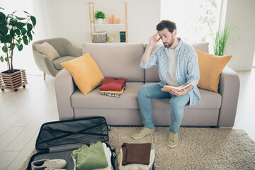 Obraz premium Photo of handsome bearded alone mature age adult man sitting indoors living room packing clothes inside valise stressed preparing for journey