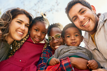 Parents, children and adoption with smile, portrait and field for fun and playing in park. Vacation, interracial family and kids with hug, together and bonding for summer holiday with confidence