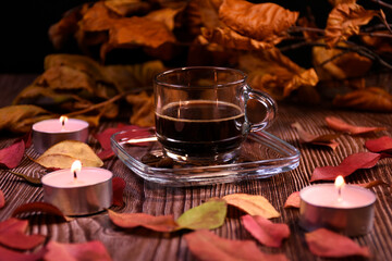 Cup of coffee, coffee beans on a saucer on a table with autumn leaves and candles. Romantic atmosphere.
