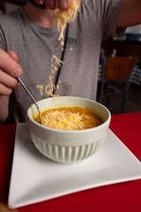 Pumpkin soup topped with a generous portion of grated cheese, served alongside a basket of bread rolls. The inviting meal is complemented by a glass of water and wine