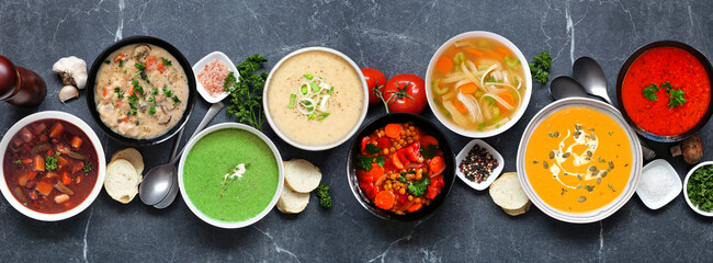 Selection of delicious homemade soups. Overhead view table scene on a dark slate banner background....