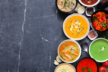 Assortment of delicious homemade soups. Above view side border on a dark slate background. Warm and cozy food concept.
