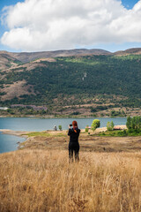 Redhaired woman takes a picture of a serene lake surrounded by mountains and open fields