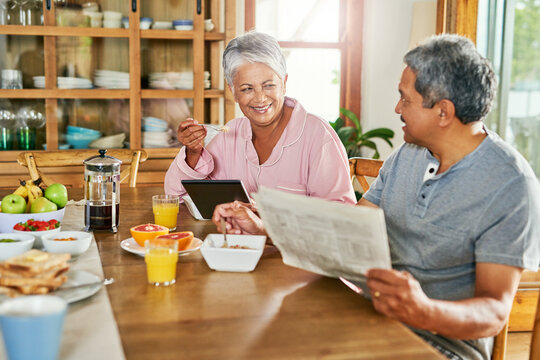 Newspaper, breakfast and senior couple with tablet, eating healthy at home and wellness and food together. Happy, conversation and old man and woman reading headlines and morning meal in house.
