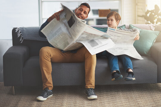 Father, kid or reading a newspaper on sofa in home for article, information or knowledge with learning. People, man or boy child with print publication on couch in living room for newsletter or story