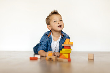 A cheerful boy lays on his stomach, engaging with vibrant wooden blocks as he constructs a tower. Natural light fills the room, enhancing the playful atmosphere.