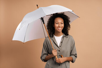 Curly African American woman with umbrella for fall season in studio on beige background