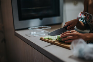 A woman is slicing fresh cucumber on a wooden cutting board in a modern kitchen. The scene depicts a focus on healthy cooking and culinary skills, with emphasis on fresh ingredients.