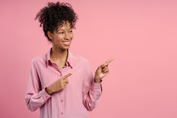 Studio portrait of smiling African American woman wearing pink shirt pointing aside