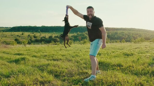 Black puppy with a toy ball on a rope in his teeth. summer day. Pinscher dog holding toy in mouth, clenching teeth, dog training, growl.Concept of pet walk, activity, dog.