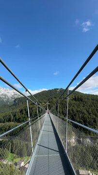 Highline 176 suspension bridge stretches over a forested valley, offering a thrilling view of the mountains under a clear blue sky.