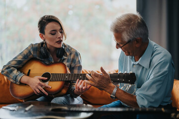 An elderly professor guides a young student in playing guitar during a music class. Together they explore musical techniques and creativity, fostering a learning environment.