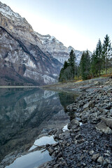 Klöntalersee in the Glarus mountains on a crisp fall morning, where the smooth surface of the water reflects the mountains.