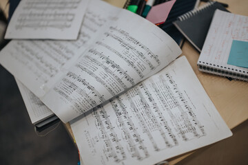 Open sheet music and notebooks are laid out on a desk, depicting students attending a music class at college. The scene captures creativity and learning.