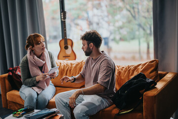Two students engaged in conversation while sitting on a comfortable orange couch. A guitar in the background adds a creative touch to the study atmosphere.