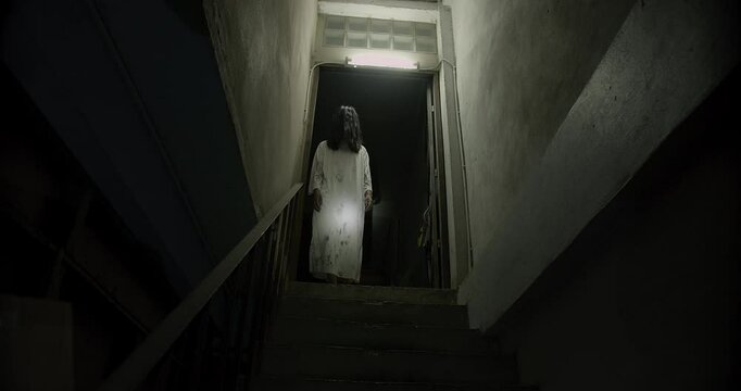 Horror scene of a mysterious Scary Asian ghost woman creepy have hair covering the face walking down on staircase at abandoned house with dark scene movie at night, festival Halloween concept