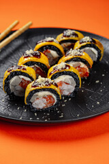 Mango-Wrapped Black Rice Sushi Rolls with Shrimp, Salmon, and Crispy Flakes on Black Plate