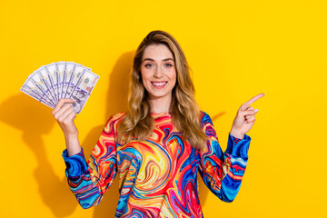 Photo portrait of pretty young girl point empty space money fan wear trendy colorful outfit isolated on yellow color background