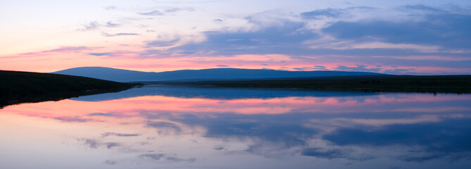 A beautiful sunset over a lake with a reflection of the sky in the water. The sky is a mix of pink and orange hues, creating a serene and peaceful atmosphere