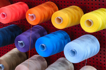 A row of colorful spools of thread hanging on a red wall. The spools are of different colors and sizes, and they are arranged in a neat and orderly fashion