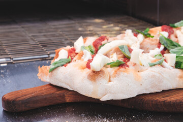 A pizza with a lot of toppings including cheese, spinach, and tomatoes. The pizza is on a wooden cutting board