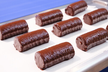 A tray of chocolate covered doughnuts. The doughnuts are all lined up and are covered in chocolate