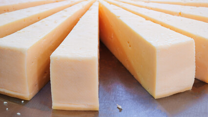 A large piece of cheese is cut into slices and placed on a metal surface. The slices are arranged in a circle, with some of them overlapping. Concept of precision and attention to detail