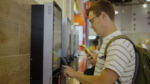 Customer interacting with a self-service checkout kiosk at a grocery store, holding a smartphone while completing a contactless payment for purchases
