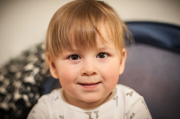 Young child with light brown hair sits smiling in cozy indoor setting wearing a playful patterned outfit in warm lighting during afternoon