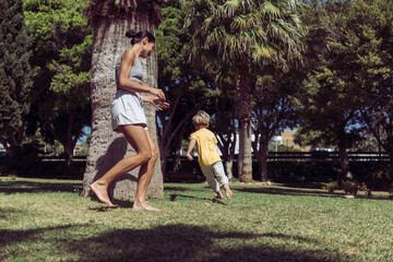 Understood, here it is: Joyful Young Mother Runs and Plays with Her Four-Year-Old Son in the Park