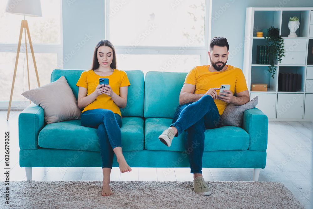 Sticker Full length portrait of two young people sit sofa use smart phone weekend pastime modern interior flat indoors