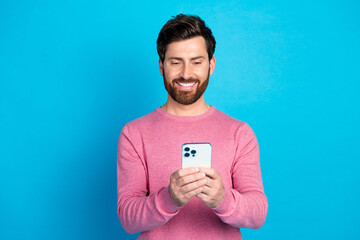 Smiling man using smartphone, enjoying technology on a bright day, isolated against blue background